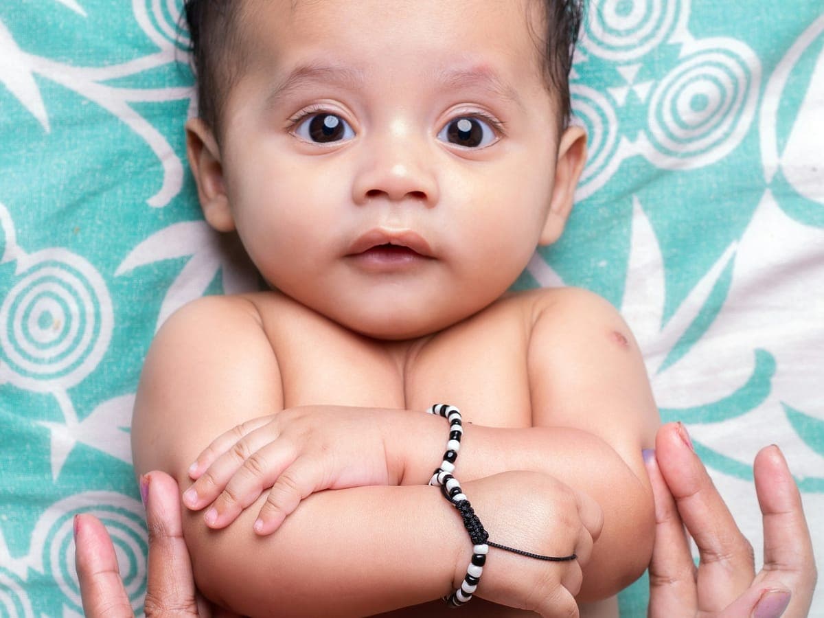 Baby lying on a blanket, held gently by an adult's hands