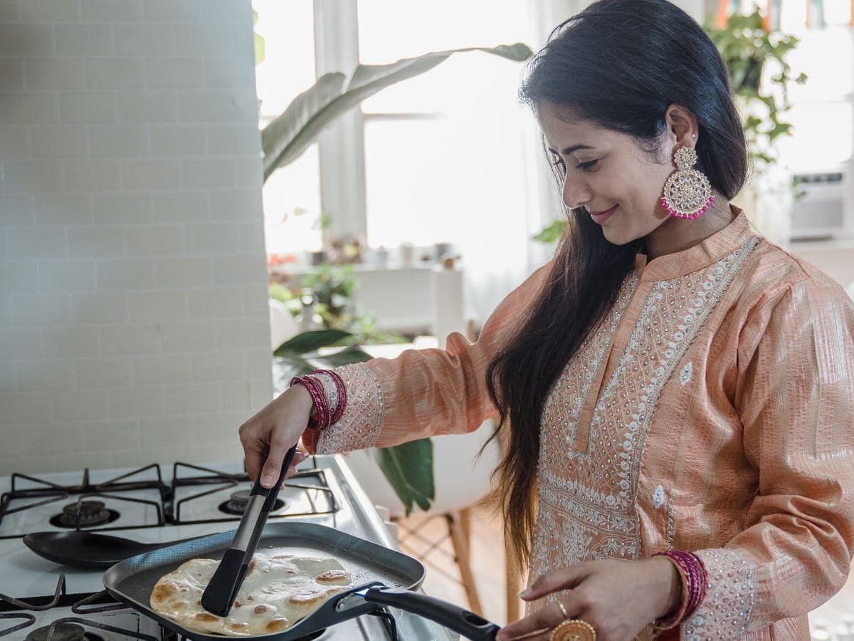 Woman cooking paratha on a gas stove at home